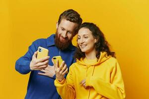 Mann und Frau Paar lächelnd fröhlich mit Telefon im Hand Sozial Medien Anzeigen Fotos und Videos, auf Gelb Hintergrund, Symbole Zeichen und Hand Gesten, Familie Freiberufler.