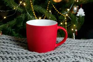 leer rot Becher mit Weihnachten Baum auf Hintergrund, Matte Tee oder Kaffee Tasse mit Weihnachten und Neu Jahr Dekoration, vertikal spotten oben mit Keramik Becher zum heiß Getränke, leer Geschenk drucken Vorlage. foto