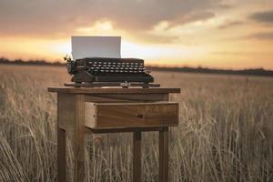 Schreibmaschine auf einem Walnuss-Nachttisch in einem Weizenfeld bei Sonnenuntergang foto