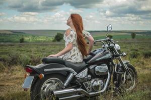 rothaariges Mädchen in einem weißen Kleid und Stiefeln zusammen mit einem Motorrad-Lavendelfeld foto