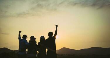 Gruppe von Menschen mit erhobenen Armen, die den Sonnenaufgang auf dem Berghintergrund betrachten. Glück, Erfolg, Freundschaft und Gemeinschaftskonzepte. foto