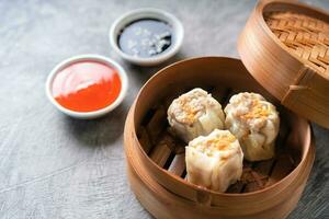 Chinesisch gedämpft Knödel oder dim Summe mit Stäbchen im Bambus Dampfer auf dunkel abstrakt Hintergrund foto