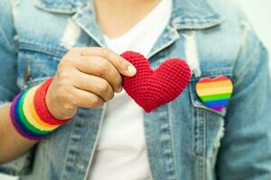 asiatische dame, die regenbogenflaggenarmbänder trägt und rotes herz hält, symbol des lgbt-stolzmonats, feiert jährlich im juni sozial für schwule, lesbische, bisexuelle, transgender, menschenrechte. foto