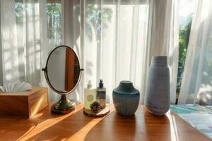 Dressing Tabelle mit Spiegel, Creme, Vase und Gewebe Box durch Weiß Vorhang foto