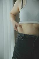 Fette Frau, dicker Bauch, mollige, fettleibige Frauenhand, die übermäßiges Bauchfett mit Maßband hält, Frauendiät-Lifestyle-Konzept foto