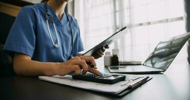 Arzt Arbeiten mit Laptop Computer und Schreiben auf Papierkram. Krankenhaus Hintergrund. foto