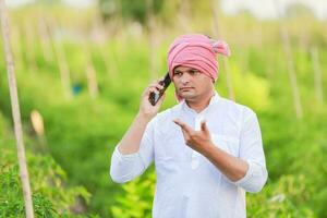 jung indisch Farmer zeigen Clever Telefon , Farmer reden auf Telefon im Bauernhof, glücklich indisch Farmer foto