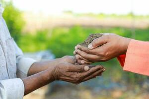 indisch Farmer halten Boden im Hände, glücklich Landwirtschaft, fallen lassen Boden im andere Hand foto