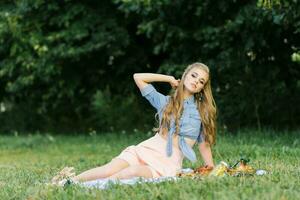 ein schön jung Frau ist Sitzung auf ein Decke auf das Gras. Sommer- Picknick foto