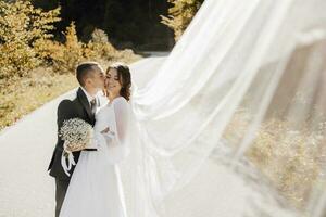 ein stilvoll Bräutigam zärtlich Küsse das Braut Wange. schön Braut mit modern Strauß Umarmen stilvoll Bräutigam im schön Licht. sinnlich romantisch Moment. Hochzeit. stilvoll und schön foto