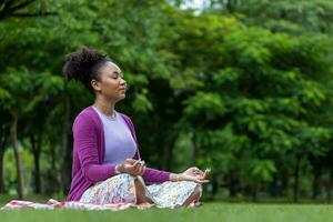 afrikanisch-amerikanische Frau, die entspannend Meditation im Wald praktiziert, um Glück aus innerer Friedensweisheit für ein gesundes Geist- und Seelenkonzept zu erlangen foto