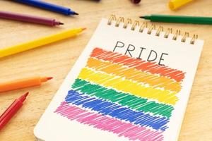 Notizbuch mit LGBT-Regenbogenflaggenzeichnung und Markierstiften auf Holztisch foto