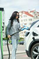 jung Geschäft Frau Auftanken ihr elektrisch Auto beim ein ev Laden Bahnhof. Konzept von ökologisch freundlich Fahrzeug. elektrisch Auto Konzept. Grün Reisen. foto