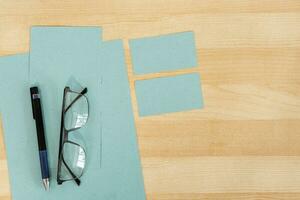 oben Aussicht von Büro Arbeit Raum, hölzern Schreibtisch Tabelle mit Brille, Blau texturiert Papier und Geschäft Karte. foto