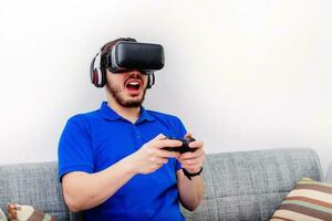Mann spielen Spiel mit virtuell Wirklichkeit Headset und Spiel Joystick im das Leben Zimmer, beim heim. foto