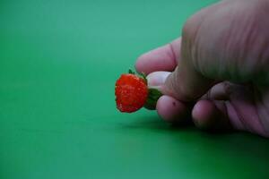 Hand halten ein gebissen Erdbeere isoliert auf Grün Hintergrund. foto
