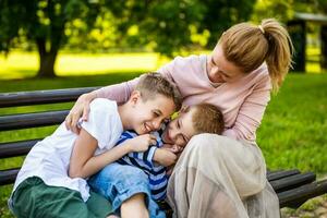 glücklich Mutter ist Sitzung mit ihr Söhne auf Bank im Park. Sie sind haben Spaß zusammen. foto