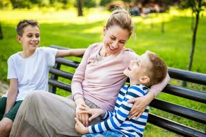 glücklich Mutter ist Sitzung mit ihr Söhne auf Bank im Park. Sie sind haben Spaß zusammen. foto