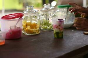 indonesisch Straße Verkäufer Hände bereiten ein Glas von Straßenrand Obst Eis wie Kunden geduldig warten zum ihr Aufträge. foto