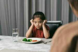 Mutter ist erzählen ihr süß Kind Essen nützlich Gemüse aber das Kind weigert sich zu essen. foto