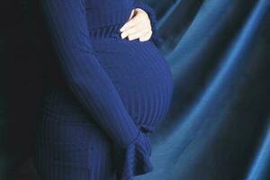Bauch der schwangeren Frau, Nahaufnahme. hände, die bauch im blauen hintergrund umarmen. Konzept der Müttergesundheit foto