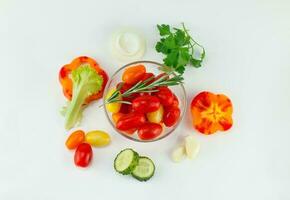 Kirsche Tomaten im ein Salat Schüssel und gehackt Gemüse um, Kopfsalat, Pfeffer, Gurken, Zwiebeln. oben Sicht, auf ein Licht Hintergrund foto