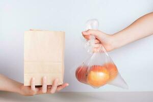 ein Hand mit ein Einweg transparent Tasche von Äpfel und ein Hand mit ein umweltfreundlich Papier Tasche foto