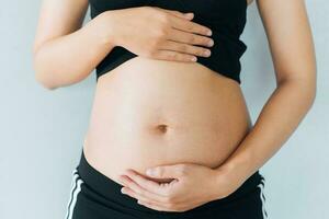 schwanger Frau hält Hände auf Bauch und Pastell- Farbe Hintergrund. Schwangerschaft, Mutterschaft, Vorbereitung und Erwartung Konzept. Nahaufnahme, Kopieren Raum. jung Frau warten zum Baby Geburt. foto