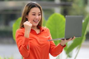 schöne junge Frau mit glücklich schreiendem überraschtem Gesicht, das Laptop in einem Stadtpark hält