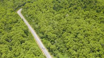 Luftbild von oben Auto, das durch den Wald auf Landstraßenansicht von Drohne fährt foto