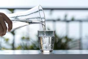 Gießen Sie im Gartenhaus Wasser aus der Flasche in ein Glas foto