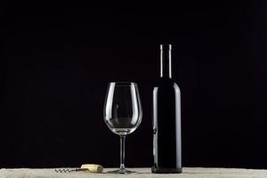 Weinflaschenglas und Korkenzieher auf einer schwarzen Hintergrundtapete