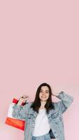 aufgeregt jung Frau im beiläufig Denim Hemd erhöht ihr Arm im Feier, Stehen im Vorderseite von ein Rosa Hintergrund, glücklich nach Einkaufen oder finden ein großartig Deal online foto
