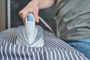 Frau bügelt Kleidung auf dem Bügelbrett mit modernem Bügeleisen foto