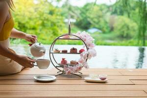 Frau Hand Gießen heiß Tee mit Nachmittag Tee einstellen und Rosa Dessert beim Luxus Hotel foto