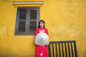 glücklich Frau tragen ao dai Vietnamesisch Kleid und Hut, Reisender Besichtigung beim hoi ein uralt Stadt, Dorf im zentral Vietnam. Wahrzeichen und Beliebt zum Tourist Sehenswürdigkeiten. Vietnam und Süd-Ost Reise Konzept foto