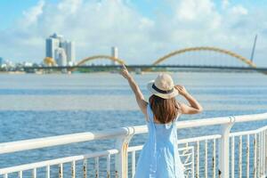 Frau Reisender mit Blau Kleid Besuch im da nang Stadt. Tourist Besichtigung das Fluss Aussicht mit Drachen Brücke. Wahrzeichen und Beliebt zum Tourist Attraktion. Vietnam und Süd-Ost Asien Reise Konzept foto