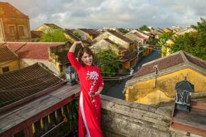 glücklich Frau tragen ao dai Vietnamesisch Kleid, Reisender Besichtigung Aussicht beim Dach im hoi ein uralt Stadt. Wahrzeichen und Beliebt zum Tourist Sehenswürdigkeiten. Vietnam und Süd-Ost Reise Konzept foto