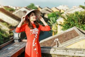 glücklich Frau tragen ao dai Vietnamesisch Kleid, Reisender Besichtigung Aussicht beim Dach beim hoi ein uralt Stadt, Dorf im Vietnam. Wahrzeichen und Beliebt zum Tourist Sehenswürdigkeiten. Vietnam und Süd-Ost Reise Konzept foto