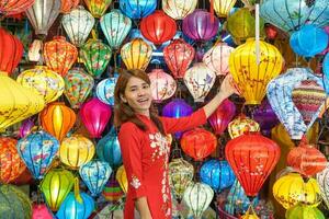 glücklich Frau tragen ao dai Vietnamesisch Kleid mit bunt Laternen, Reisender Besichtigung beim hoi ein uralt Stadt, Dorf im zentral Vietnam.Wahrzeichen zum Tourist Attraktionen.vietnam und Süd-Ost Reise Konzept foto