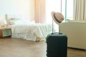 Schwarzes Gepäck mit Hut im modernen Hotelzimmer nach Türöffnung. gepäck für reisezeit, service, reise, reise, sommerferien und urlaubskonzepte foto