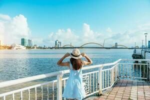 Frau Reisender mit Blau Kleid Besuch im da nang Stadt. Tourist Besichtigung das Fluss Aussicht mit Drachen Brücke. Wahrzeichen und Beliebt zum Tourist Attraktion. Vietnam und Süd-Ost Asien Reise Konzept foto