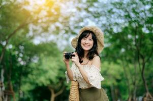 Porträt von asiatisch jung Frau Reisender mit Weberei Hut und Korb und ein Kamera auf Grün Öffentlichkeit Park Natur Hintergrund. Reise Ausflug Lebensstil, Welt Reise Forscher oder Asien Sommer- Tourismus Konzept. foto