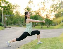 weiblich Jogger. passen jung asiatisch Frau mit Grün Sportbekleidung Dehnen Muskel im Park Vor Laufen und genießen ein gesund draussen. Fitness Läufer Mädchen im Öffentlichkeit Park. Wellness Sein Konzept foto