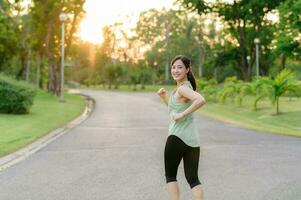 passen asiatisch jung Frau Joggen im Park lächelnd glücklich Laufen und genießen ein gesund draussen Lebensstil. weiblich Jogger. Fitness Läufer Mädchen im Öffentlichkeit Park. gesund Lebensstil und Wellness Sein Konzept foto