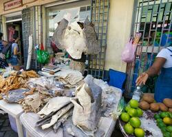 mahe Seychellen 26.06.2023 dunkel Haut Mann Verkauf gesalzen Fische in der Nähe von das Stadt, Dorf Markt im Viktoria, halten ein enorm getrocknet und gesalzen Hai Haut im seine Hand foto