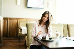 jung schön Brünette Frau sitzen im Kaffee Geschäft Cafe Restaurant drinnen und Essen Schokolade Brownie Dessert Kuchen. foto