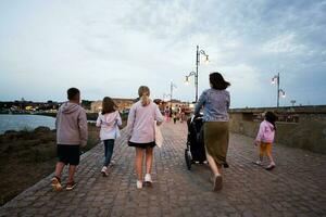 Gruppe von Kinder mit Mutter Gehen auf das Promenade im das Abend Nessebar, Bulgarien. foto