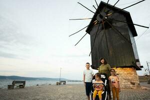 Mutter mit Kinder Stehen im Vorderseite von ein Windmühle auf das Strand Nessebar. foto