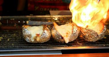 ganze Kartoffel im Aluminium Blatt, Schnitt beim Mitte Birne gebacken auf Metall Gitter über Metall Tablett. Feuer Grillen Käse auf oben von Kartoffel. foto